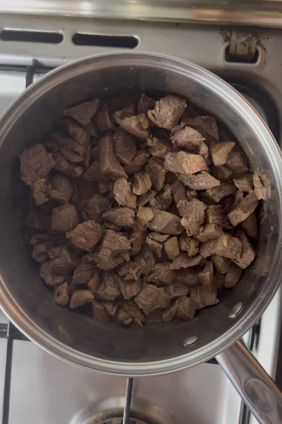 A stainless steel pot containing cooked, diced beef for a homemade beef stew for dogs sits on a stovetop.