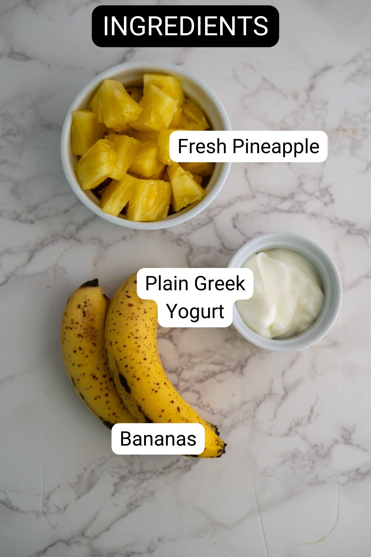 A bowl of pineapple chunks, a small dish of plain Greek yogurt, and two bananas on a marble surface—perfect ingredients for making homemade banana dog treats.