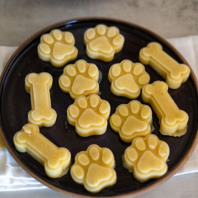 A plate with banana dog treats shaped like paws and bones, arranged in a circular pattern on a dark round dish.