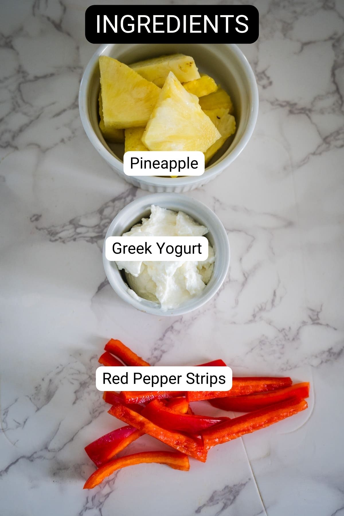 Bowls of pineapple and Greek yogurt, along with red pepper strips, are laid out on a marble surface as key ingredients for making refreshing pupsicles.