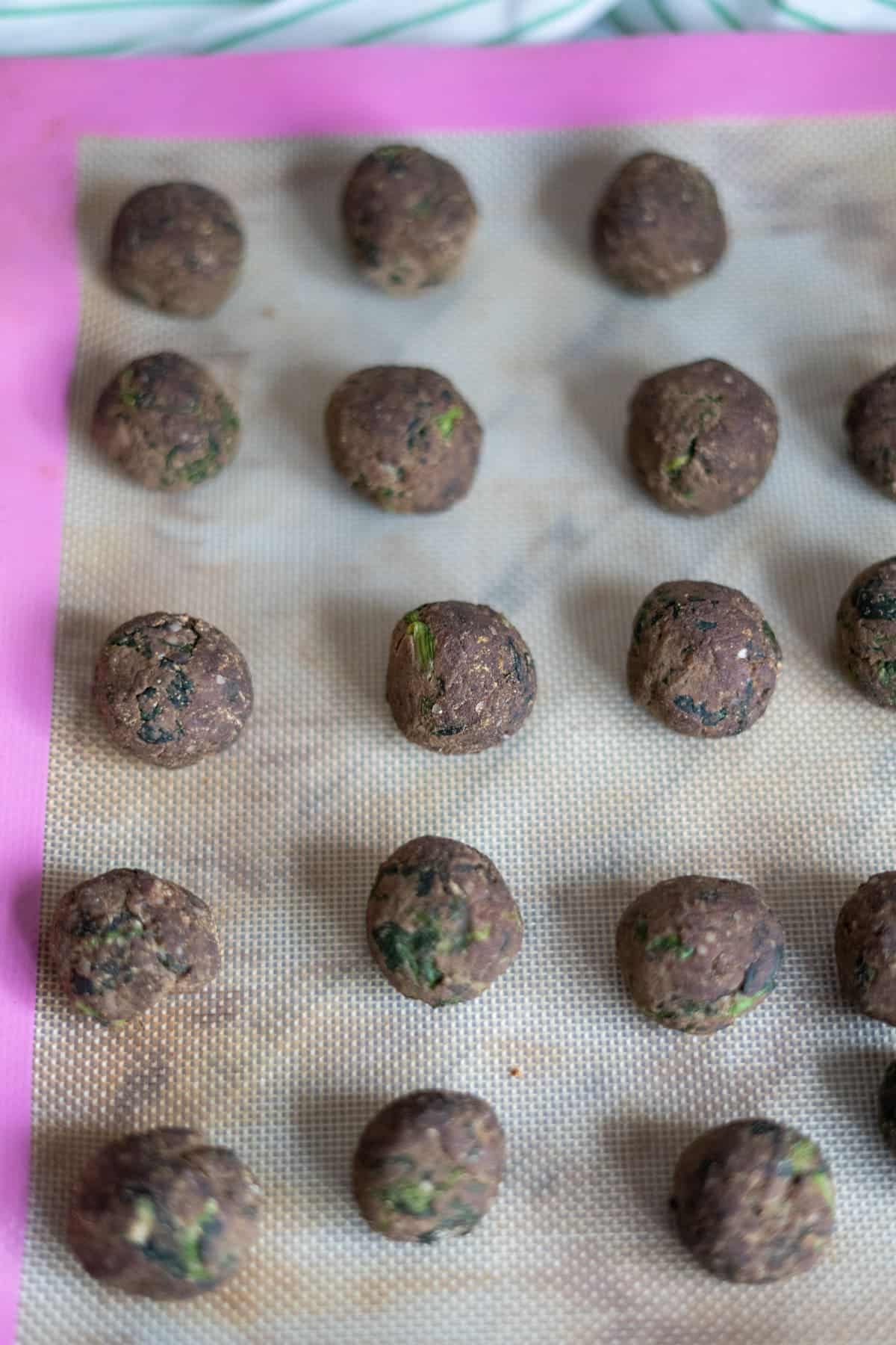 Raw falafel balls arranged on a silicone baking mat, spaced evenly in rows like chicken liver meatballs for dogs, ready to be baked or fried.
