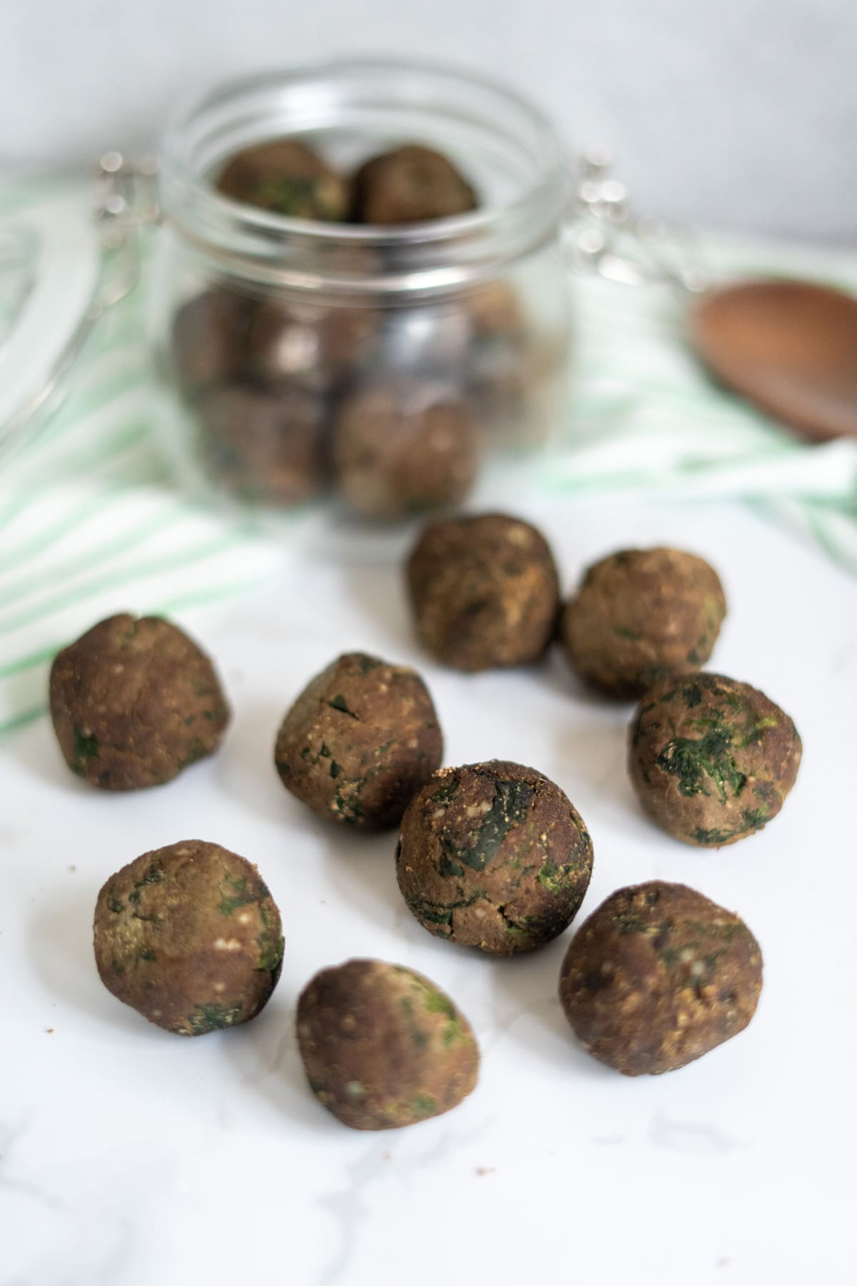 Round, brown chicken liver meatballs for dogs are arranged on a white surface, with more visible inside a glass jar in the background.