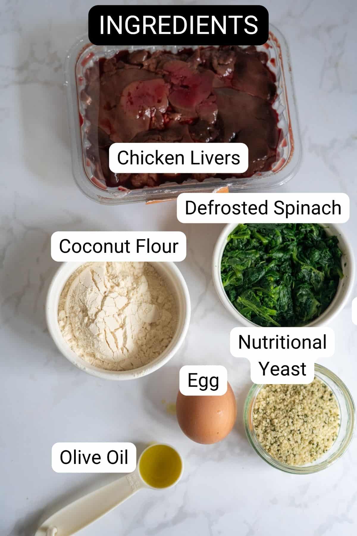 A flat lay of labelled ingredients on a white surface for chicken liver meatballs for dogs: chicken livers, defrosted spinach, coconut flour, nutritional yeast, egg, and olive oil.