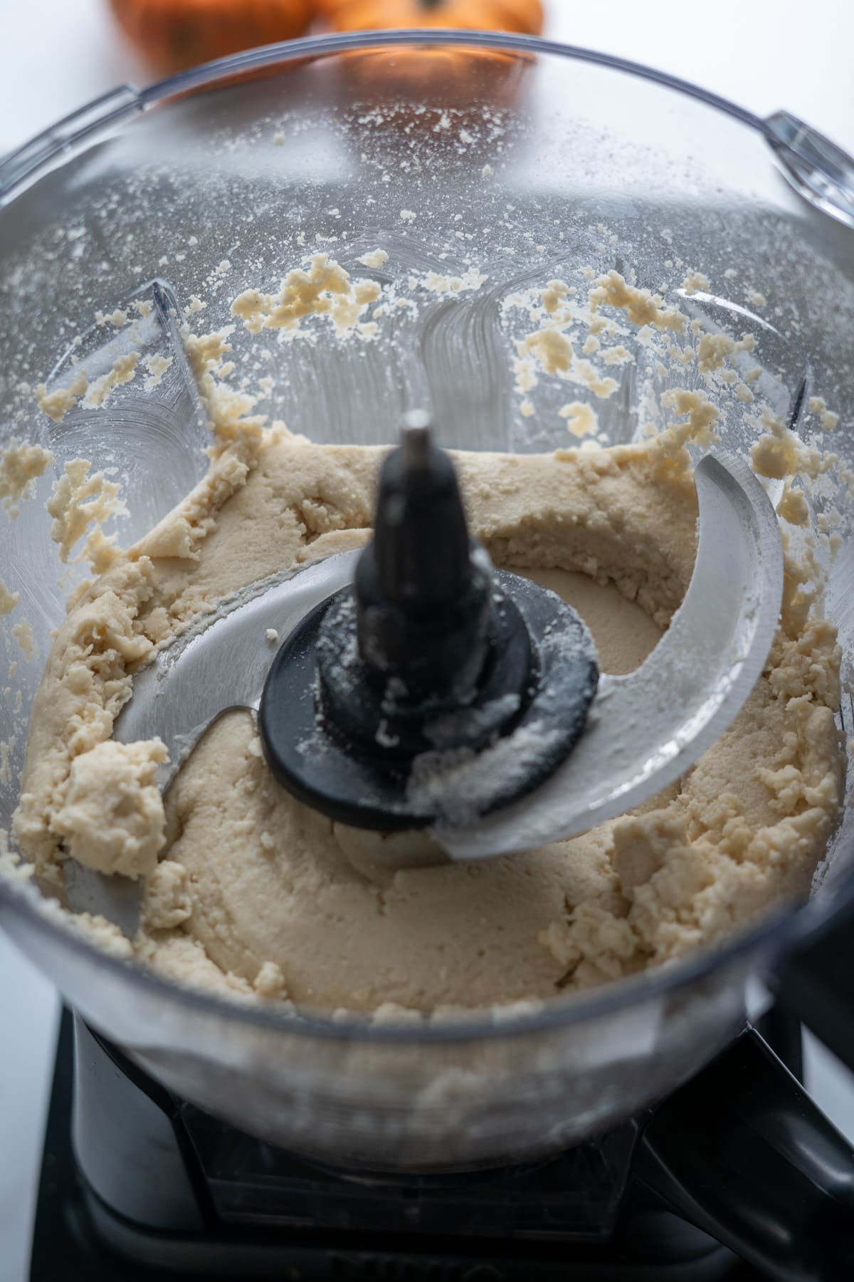 A food processor bowl containing thick, blended dough for pumpkin pies for dogs, with a metal blade in the center.