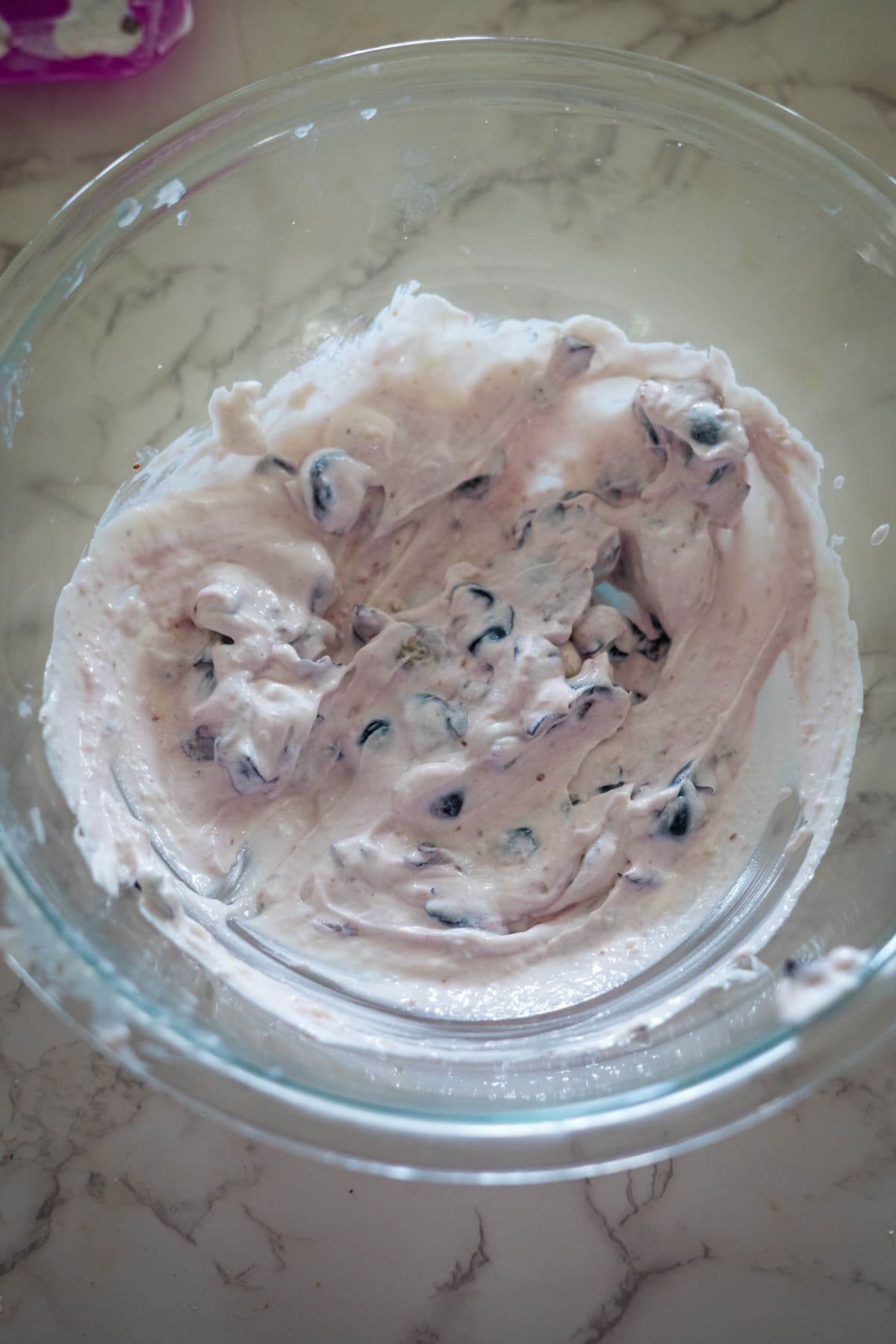 A glass bowl filled with creamy blueberry yogurt mixed with dark berries sits on a marble countertop, almost looking like the perfect mix for gourmet dog treats.