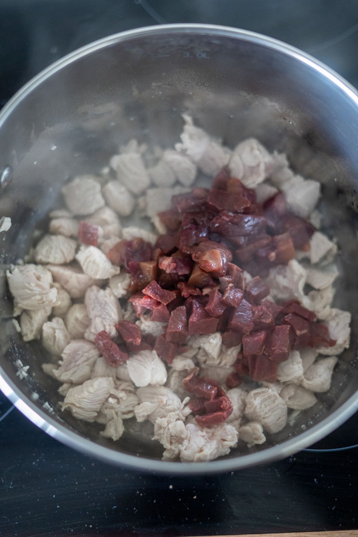 Cubed pieces of cooked chicken breast and diced sausage are heating together in a stainless steel saucepan on a hob, making it perfect for adding to your turkey dog food recipe.