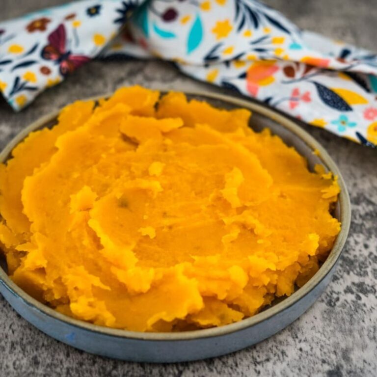 A bowl of mashed butternut squash with a floral-patterned cloth in the background.