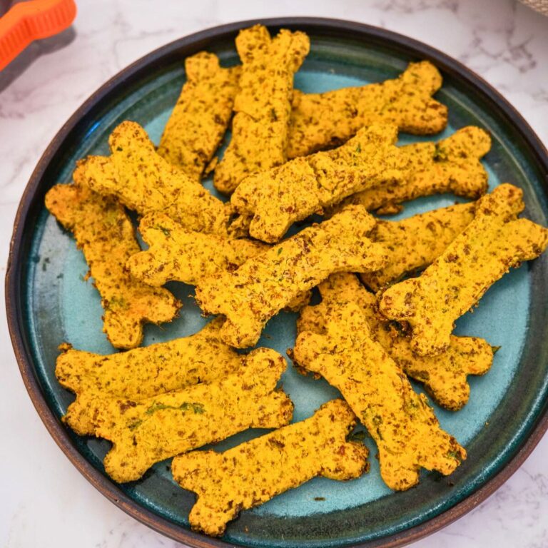A plate filled with bone-shaped, golden-yellow colored biscuits on a marble surface.
