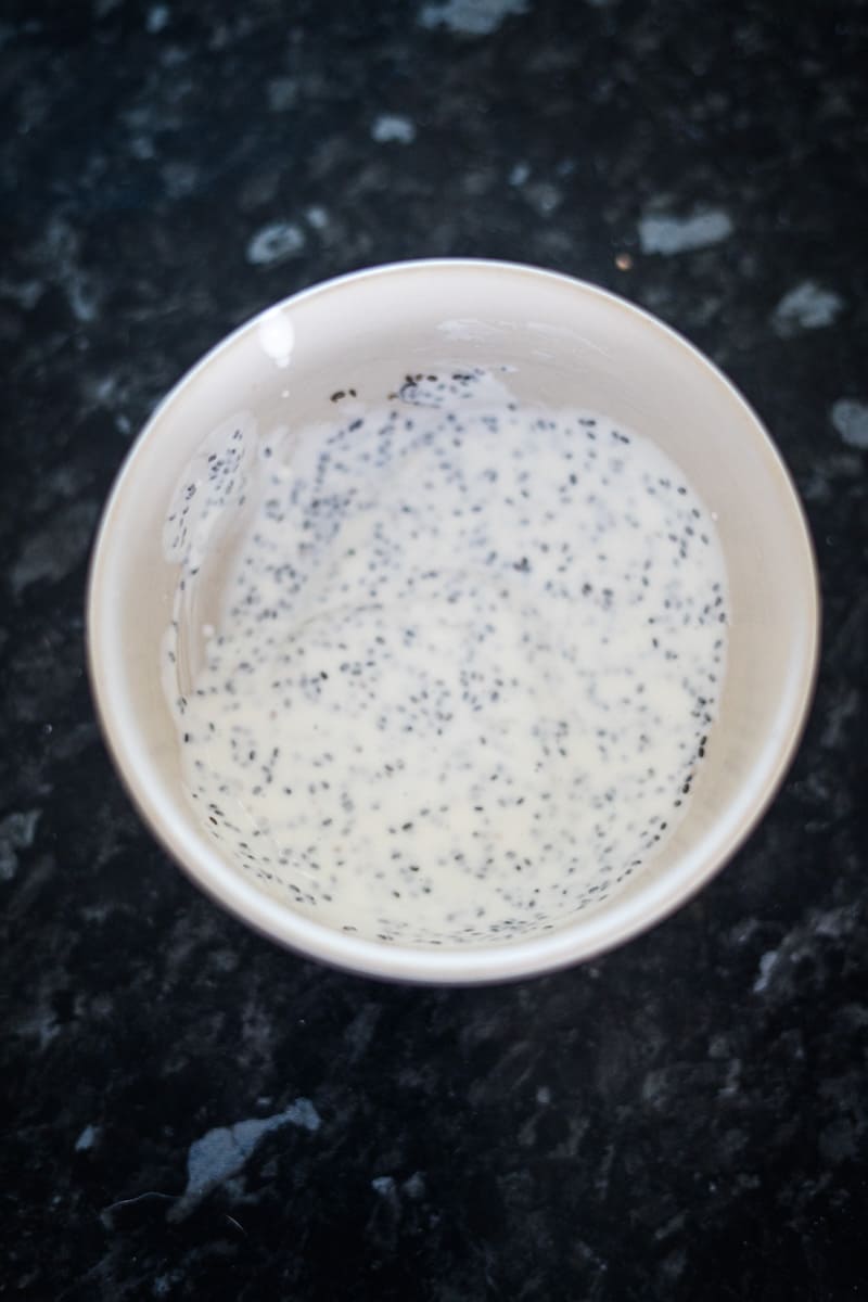 A bowl of creamy white chia pudding with visible chia seeds, placed on a dark granite surface.