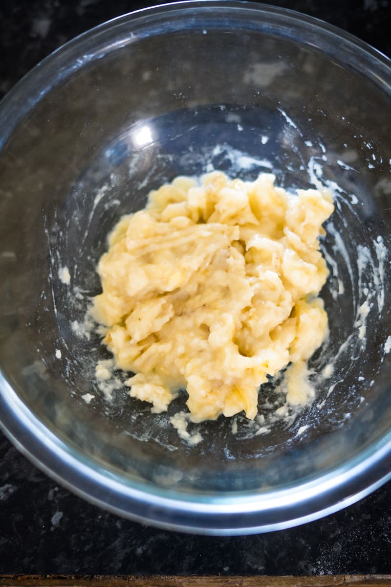 Mashed bananas in a clear glass bowl on a dark countertop.