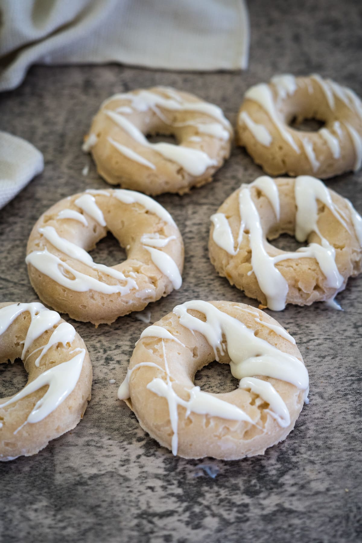 Six doggie donuts with white icing drizzled on top, arranged on a textured grey surface.