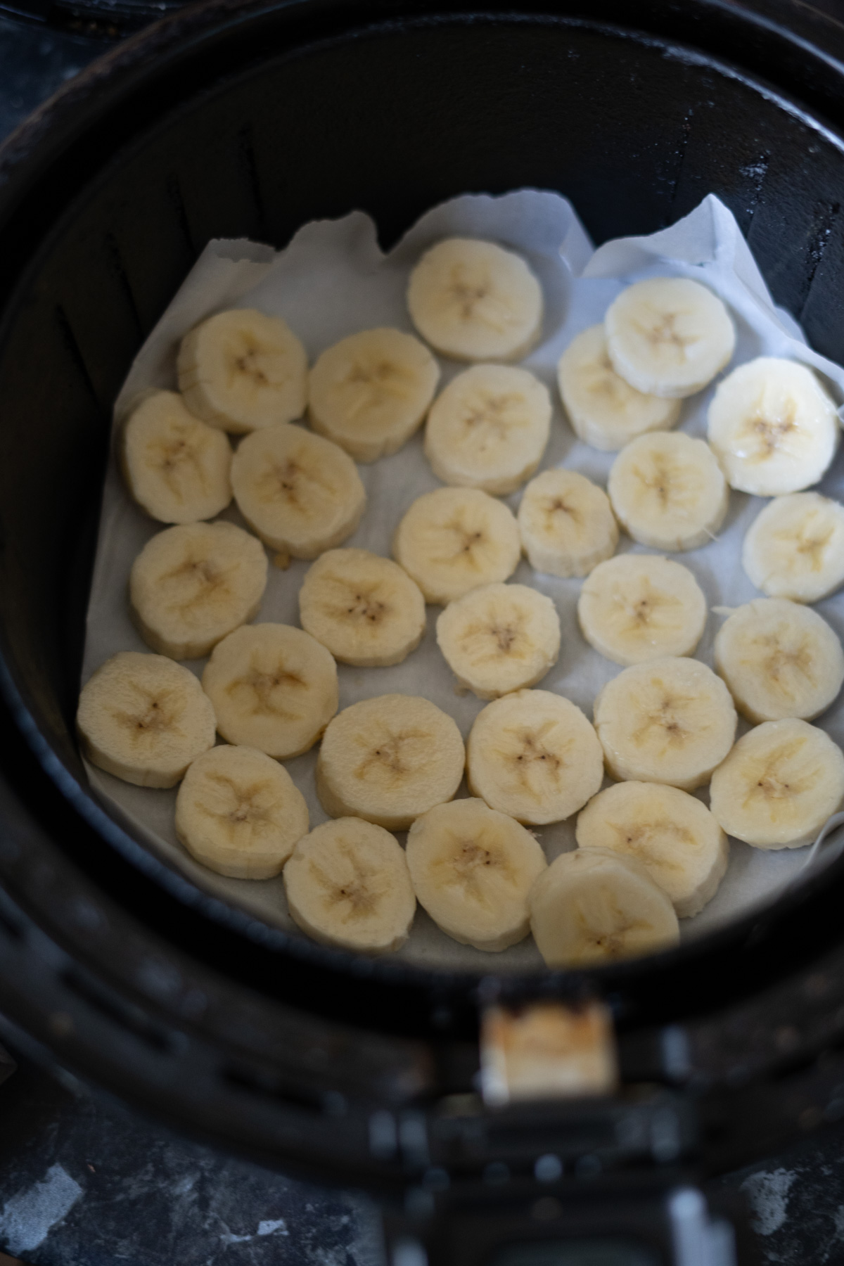 Sliced bananas arranged in a single layer on parchment paper inside an air fryer basket.