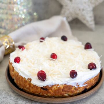A cake topped with white frosting, grated coconut, and red berries, displayed on a brown plate. A decorative star and a cloth napkin are in the background.