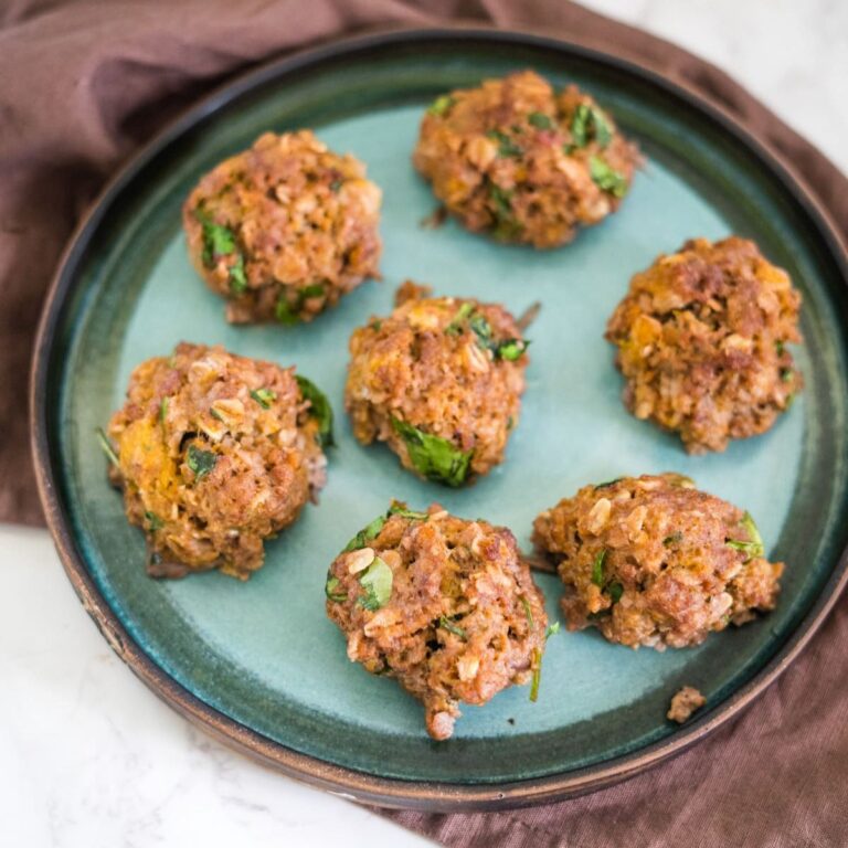 A plate with six baked falafel balls containing visible herbs and vegetables, placed on a green and brown ceramic dish.