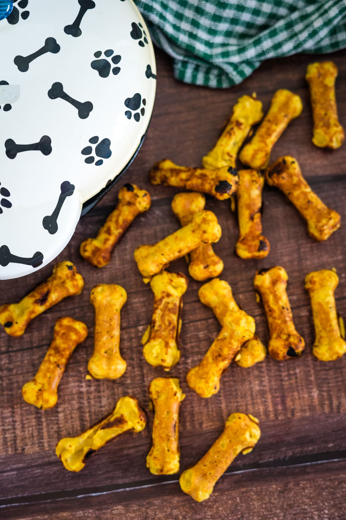 A dog-themed bowl and scattered bone-shaped dog treats on a wooden surface.