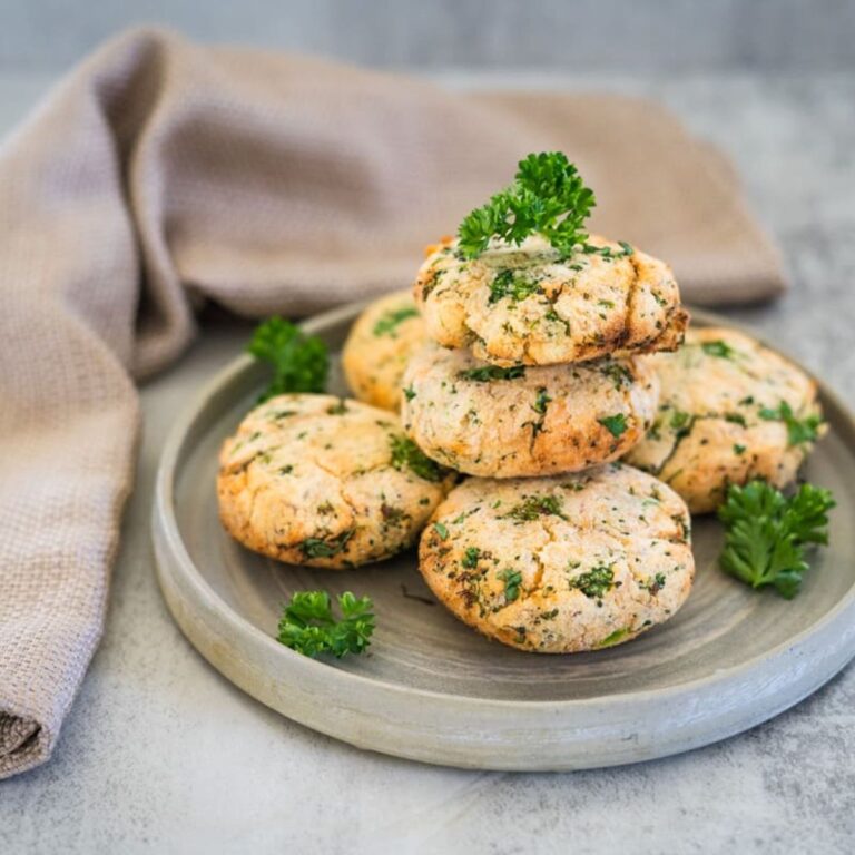 A plate with five herb biscuits stacked and garnished with parsley. A beige cloth is in the background on a gray surface.
