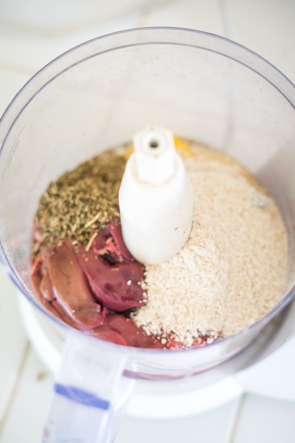 Food processor containing chicken liver, oats, and herbs before blending.