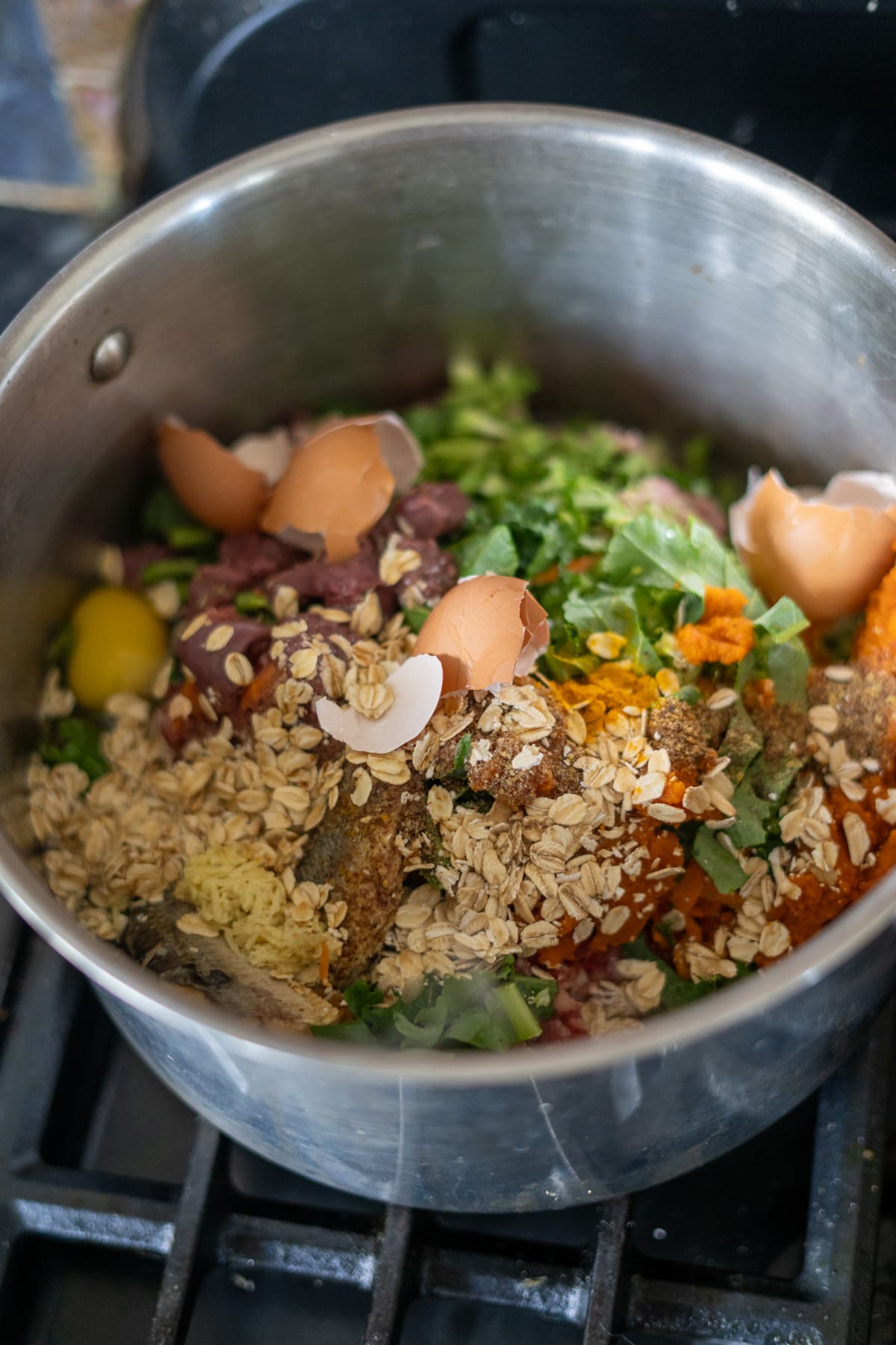 A pot on the stove simmers with a turkey dog food recipe, containing oats, egg shells, green leafy vegetables, yellow spheres resembling yolks, and other mixed contents.