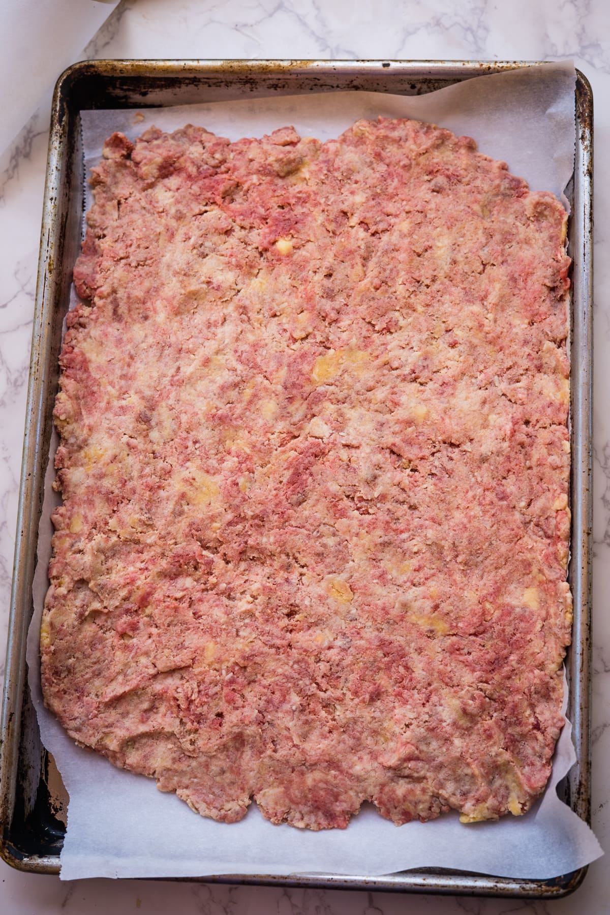Ground beef mixture, perfect as beef treats for dogs, spread flat on a parchment-lined baking sheet.