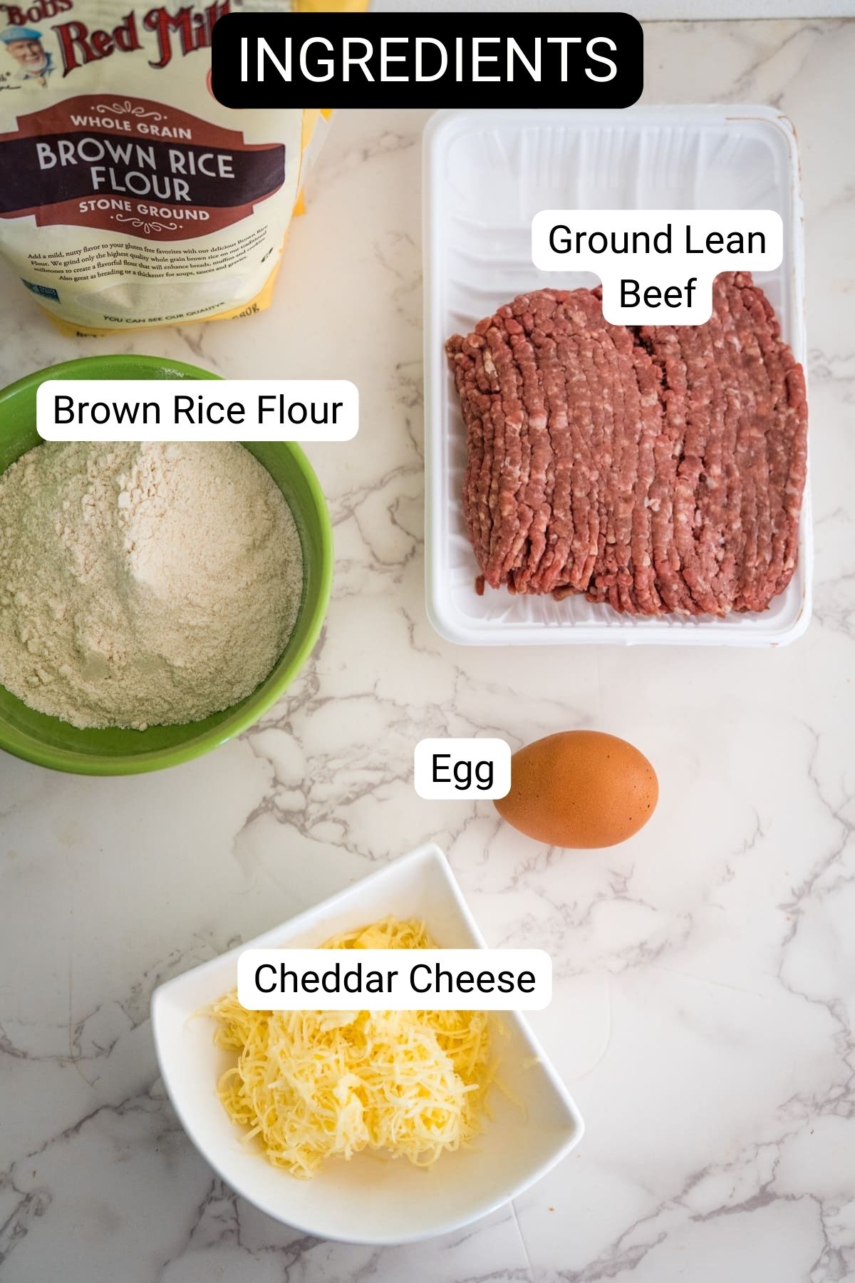 Ingredients on a marble countertop: a bag of brown rice flour, ground lean beef in a tray ready for delicious beef treats for dogs, an egg, shredded cheddar cheese in a bowl, and another bowl of brown rice flour.