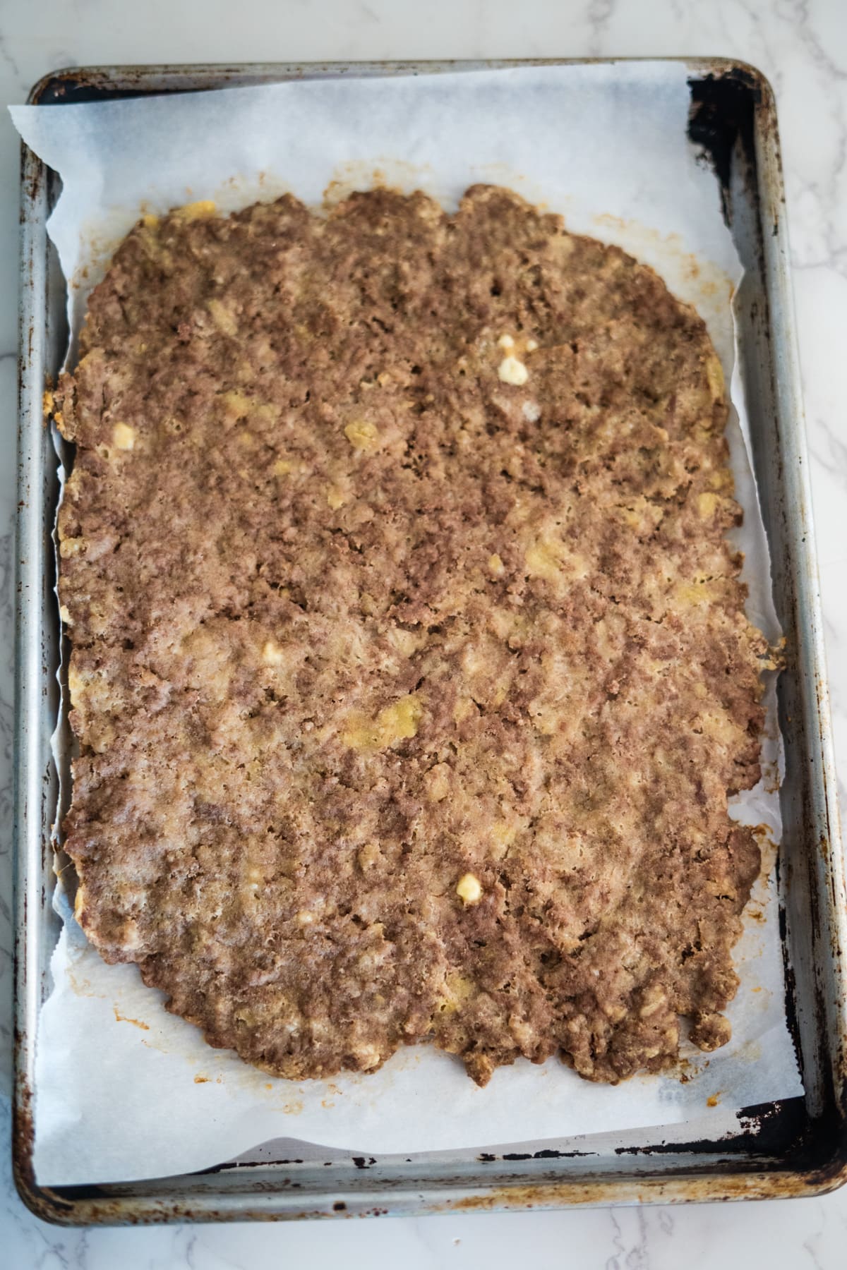 A raw beef treat mixture, perfect for dogs, is spread on a parchment-lined baking sheet, ready for cooking.