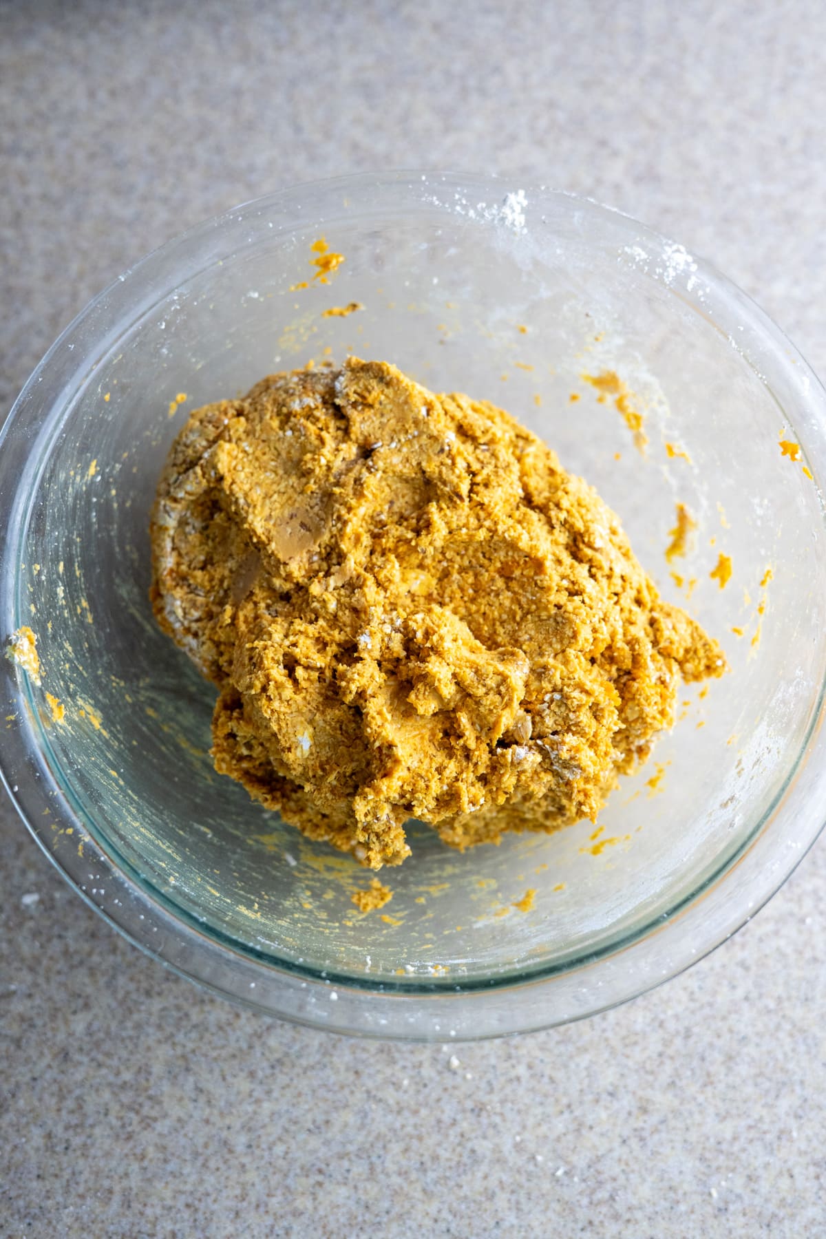 A glass bowl on a countertop contains a mound of yellowish dough, ready to become no-bake pumpkin dog treats.