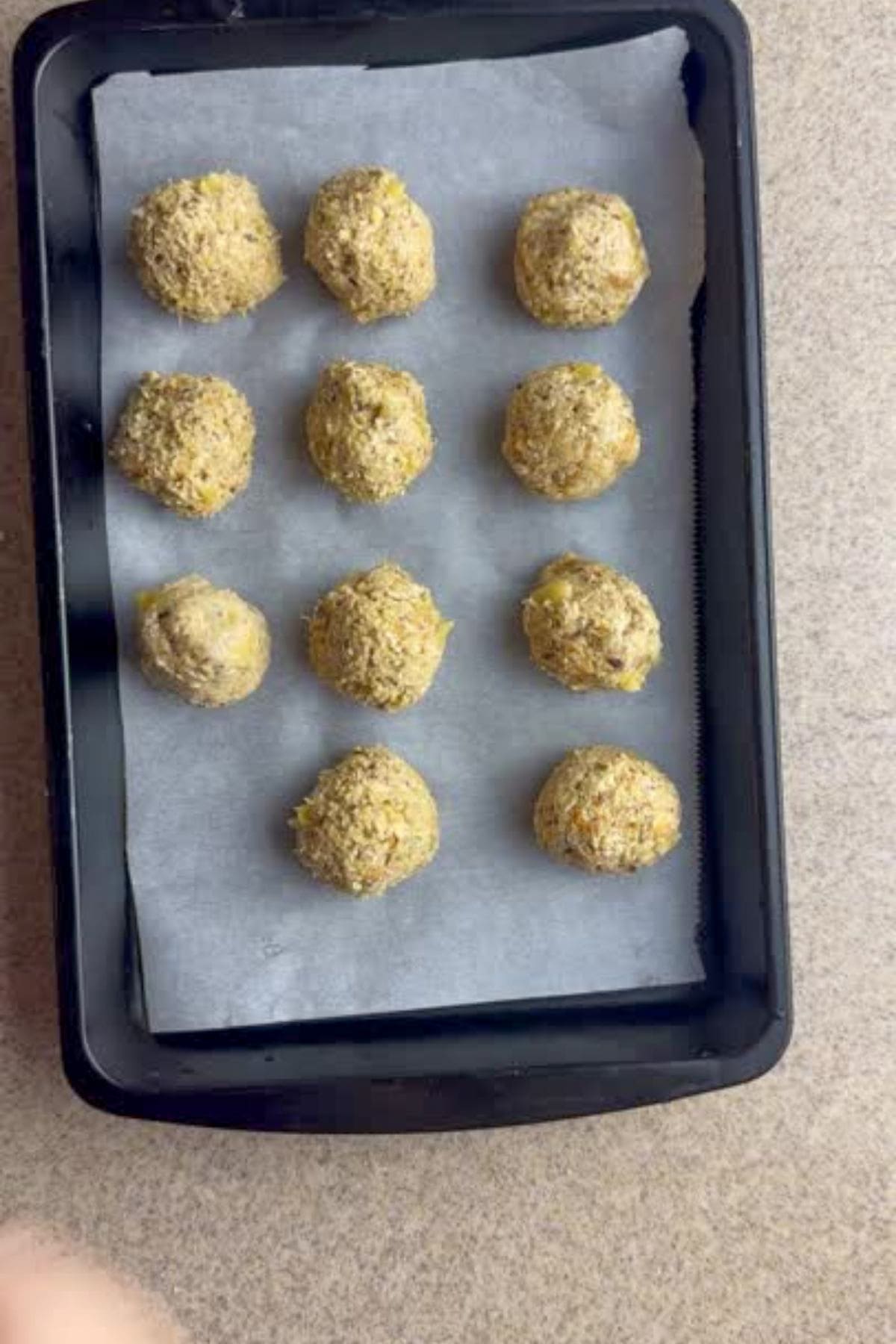Twelve round dough balls on a parchment-lined baking tray placed on a countertop.