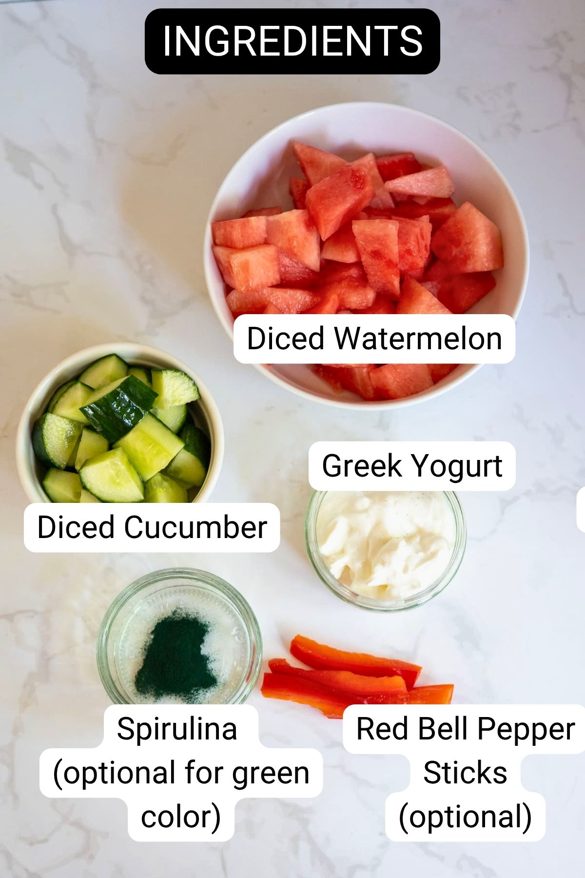 Five ingredients on a white surface: diced watermelon, diced cucumber, Greek yoghurt, spirulina powder, and red pepper sticks—each in separate bowls or piles and labelled for identification—perfect for making refreshing watermelon frozen dog treats.