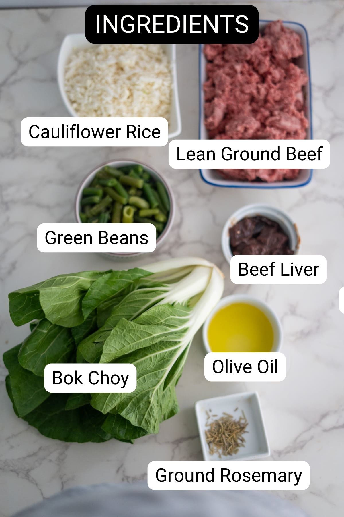 A top-down view of labeled ingredients on a marble surface: cauliflower rice, lean ground beef, green beans, beef liver, bok choy, olive oil, and ground rosemary.