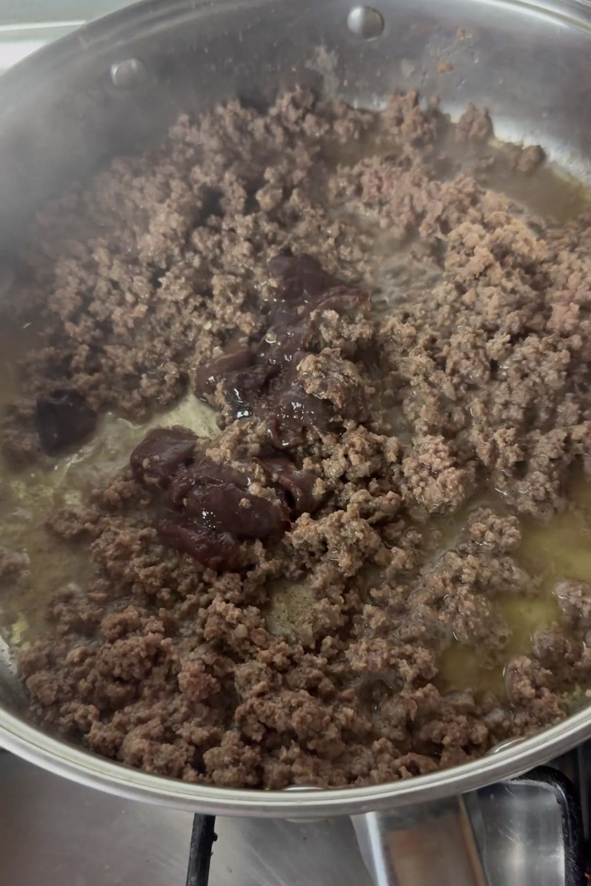 Ground meat is being cooked in a pan with juices and a darker ingredient or sauce added to the center.