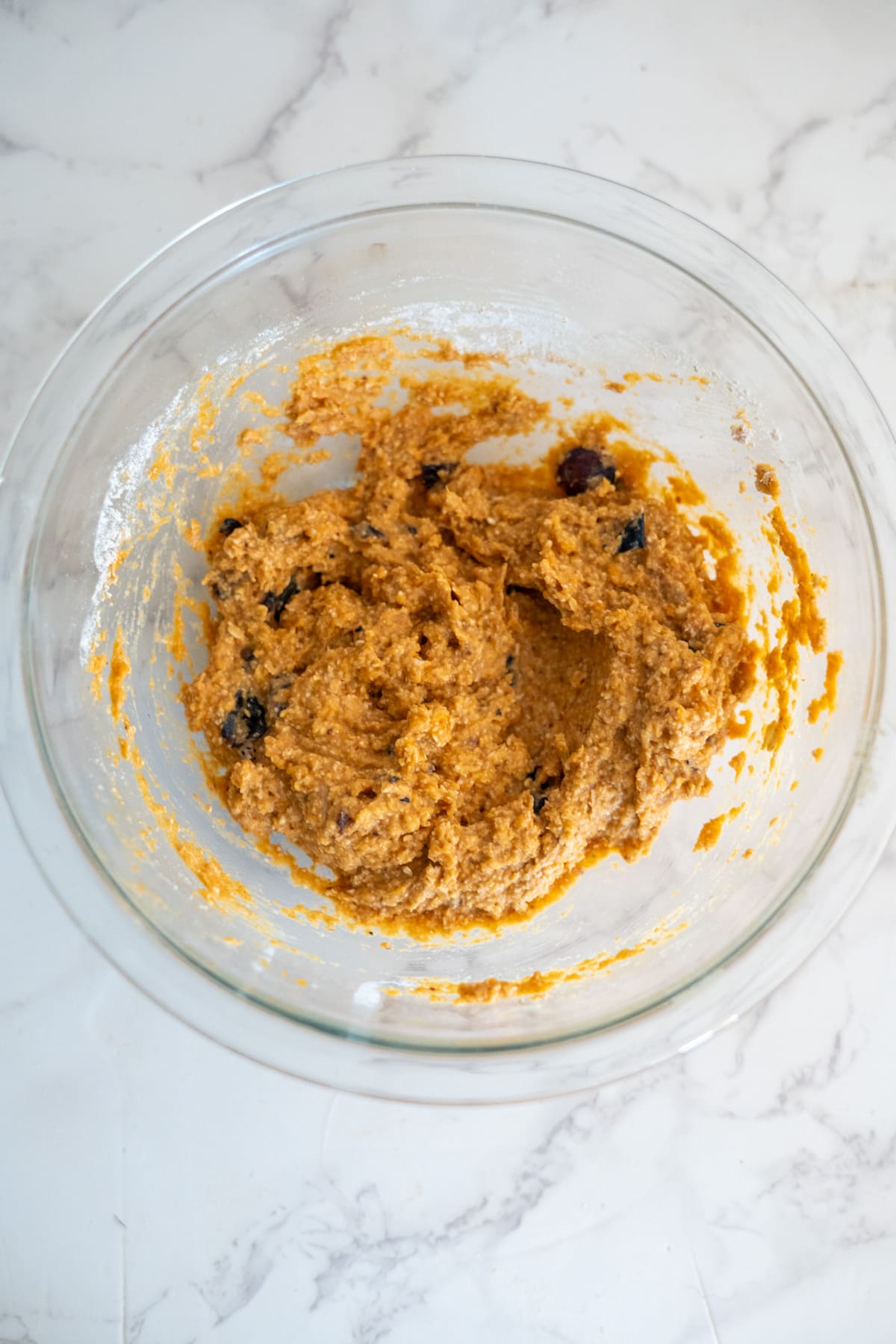 A glass bowl filled with cookie dough mixed with chocolate chips, placed on a white marble countertopโperfect for baking or even making homemade dash dog treats.