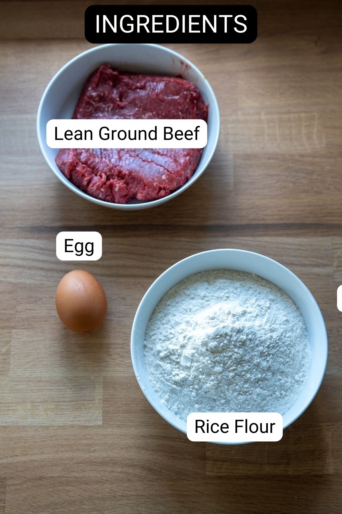 A bowl of lean ground beef, a bowl of rice flour, and a whole egg are arranged on a wooden surface, labeled as ingredients for homemade beef dog treats.