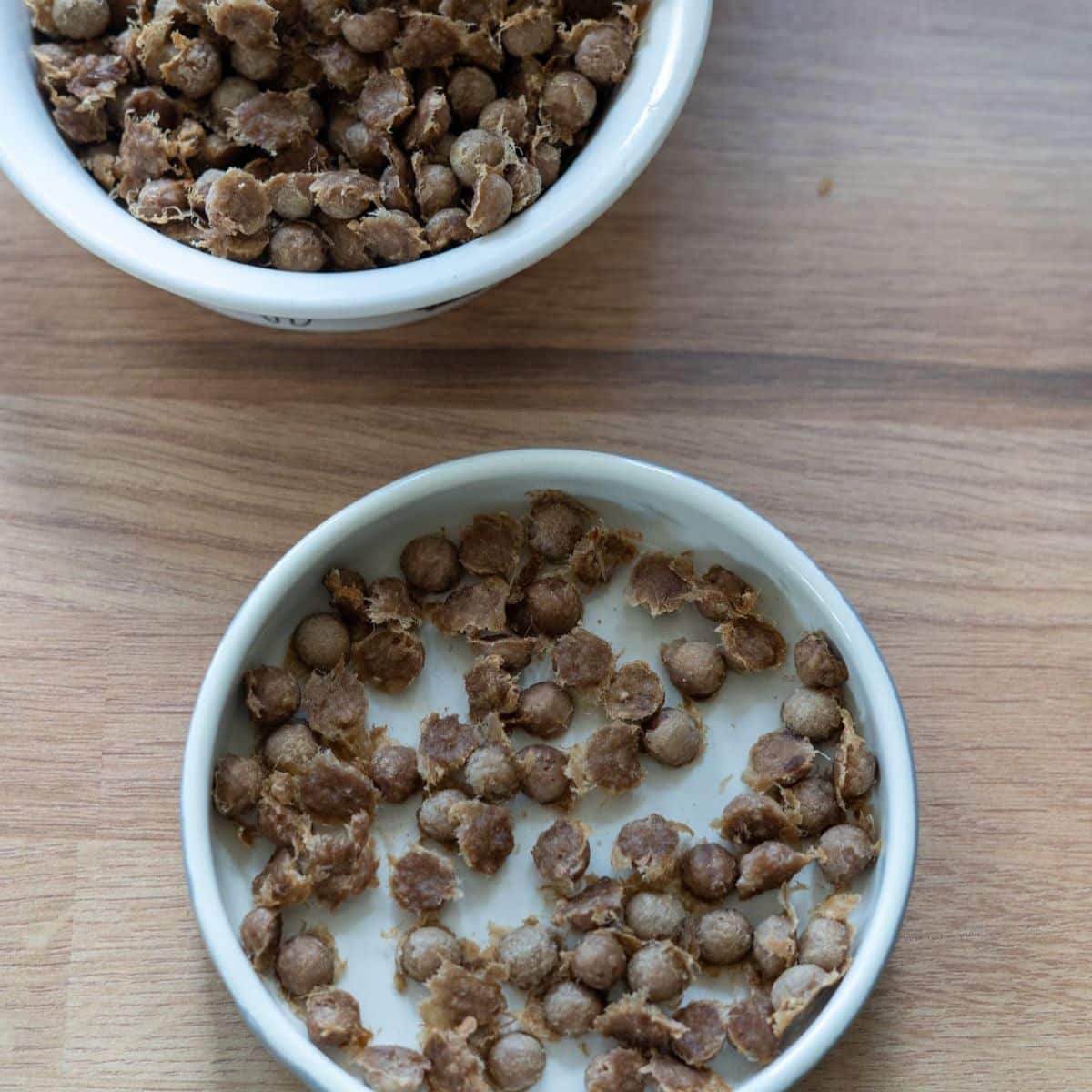 Two white bowls containing kibble soaked in water are placed on a wooden surface.