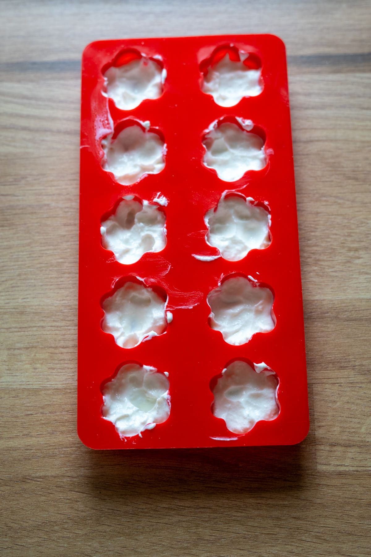 A red silicone mold tray filled with a white creamy substance, placed on a wooden surface.