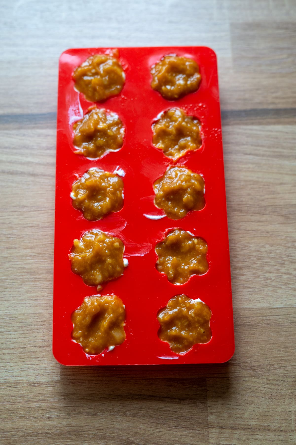 A red silicone mold filled with a brownish-orange mixture, placed on a wooden surface.