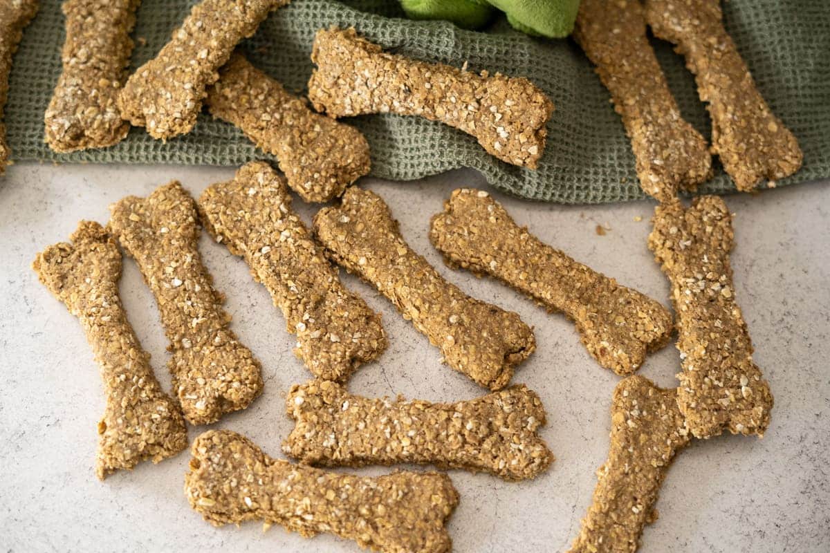 Bone-shaped oat dog biscuits spread on a countertop with a green textured cloth in the background.