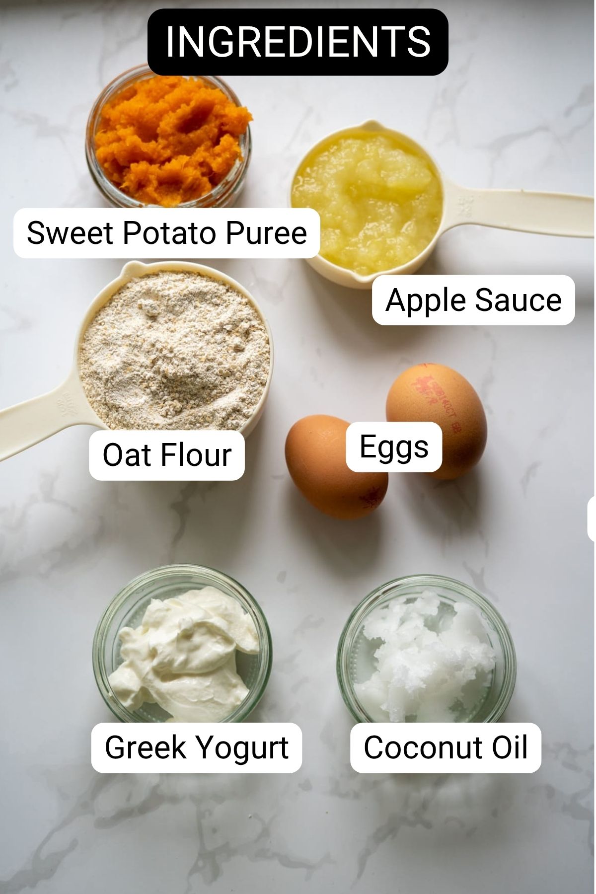 Six labeled ingredients on a white surface: sweet potato puree, applesauce, oat flour, eggs, Greek yogurt, and coconut oil.