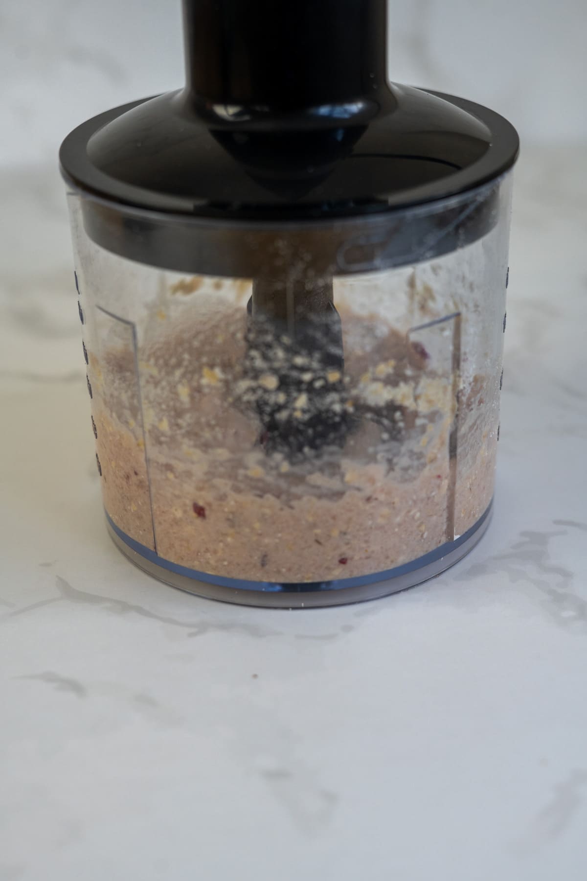 A close-up of a food processor blending a mixture of ingredients into a coarse paste on a white countertop.