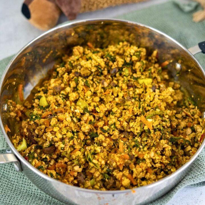 A stainless steel pan filled with a cooked mixture of crumbled tofu, vegetables, and spices sits on a green cloth.
