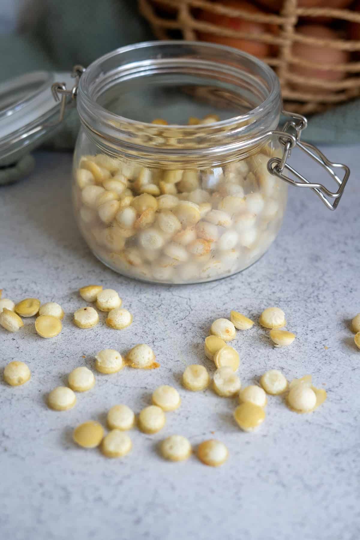 A glass jar filled with dog egg treats sits open on a gray countertop, with additional treats scattered around it.