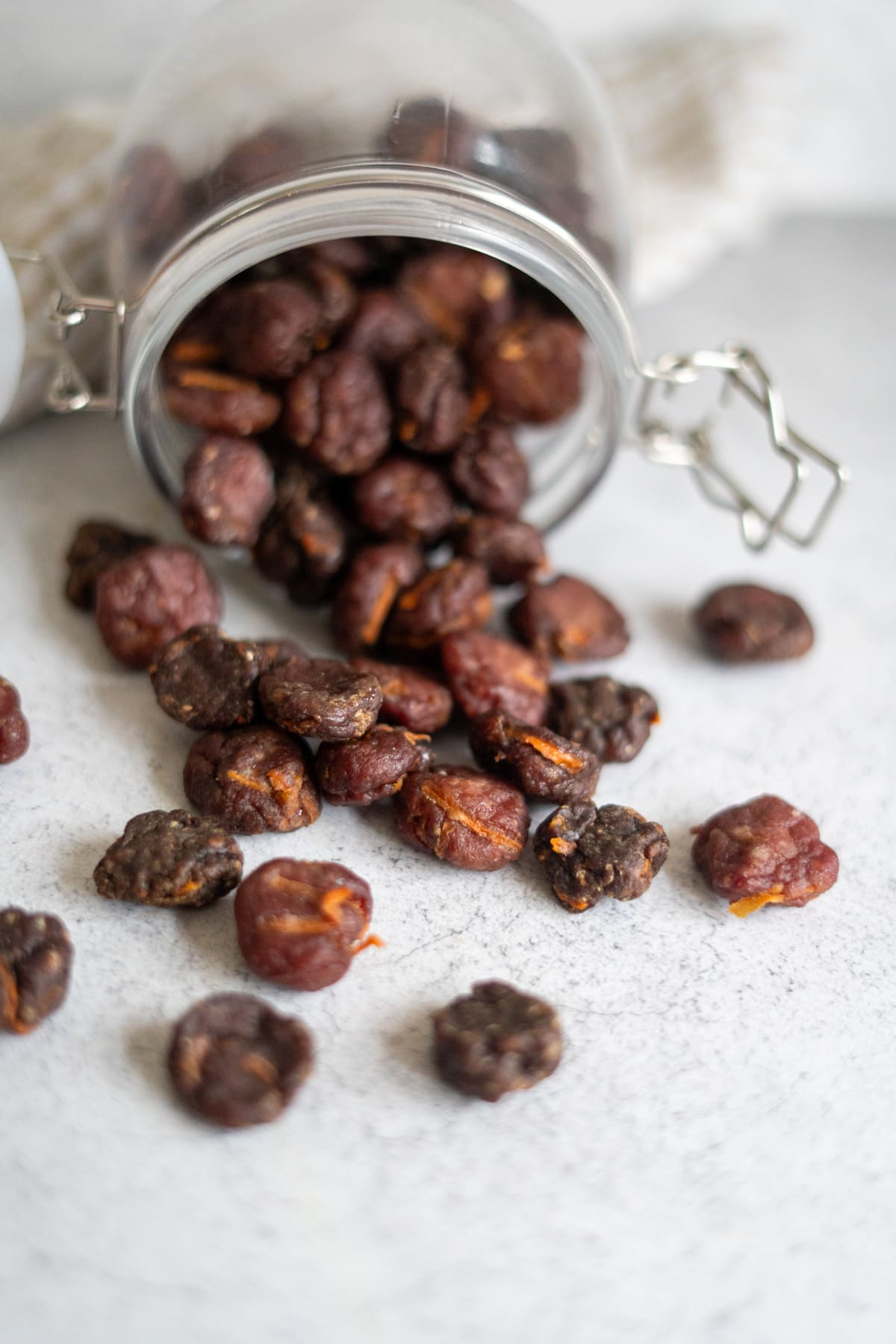 A glass jar tipped over with dried plums spilling out onto a white surface.