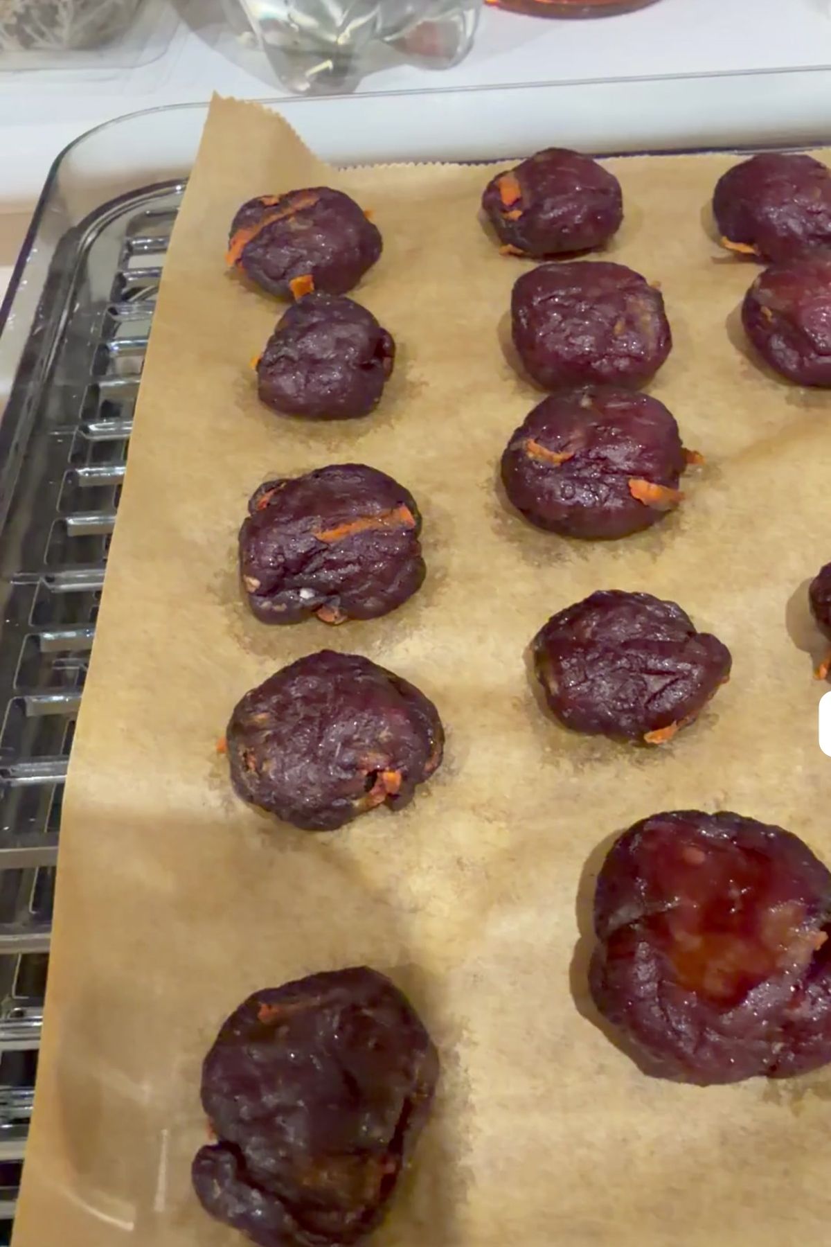 Fourteen round dark reddish dough balls with orange flecks are arranged on parchment paper on a baking tray.