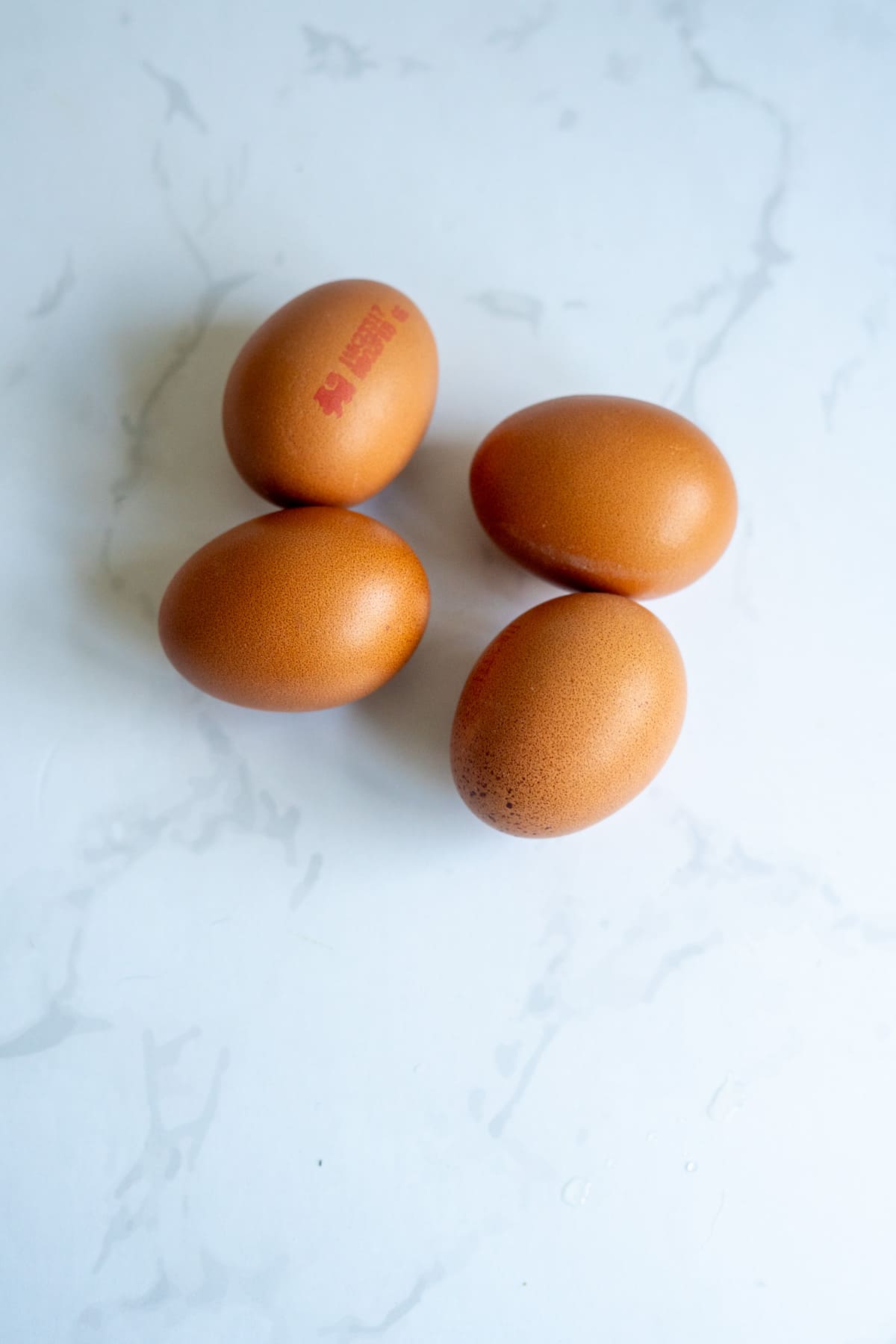 Four brown eggs, perfect for making homemade dog egg treats, are arranged on a white marble surface.