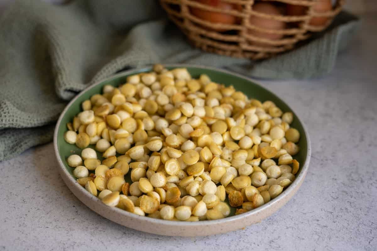 A plate filled with roasted and peeled lupini beans sits on a countertop, with a green cloth and basket in the background.