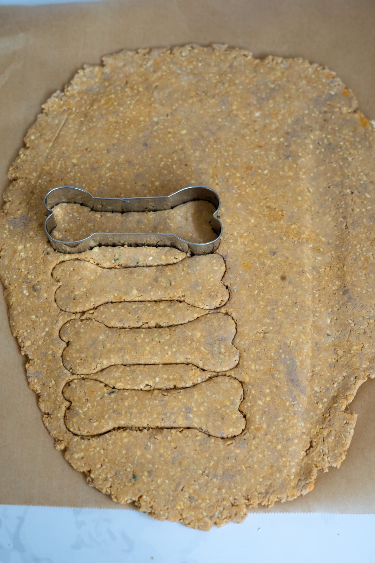 Bone-shaped biscuit cutters pressing into rolled-out dough on baking parchment, with several bone shapes already cut out.
