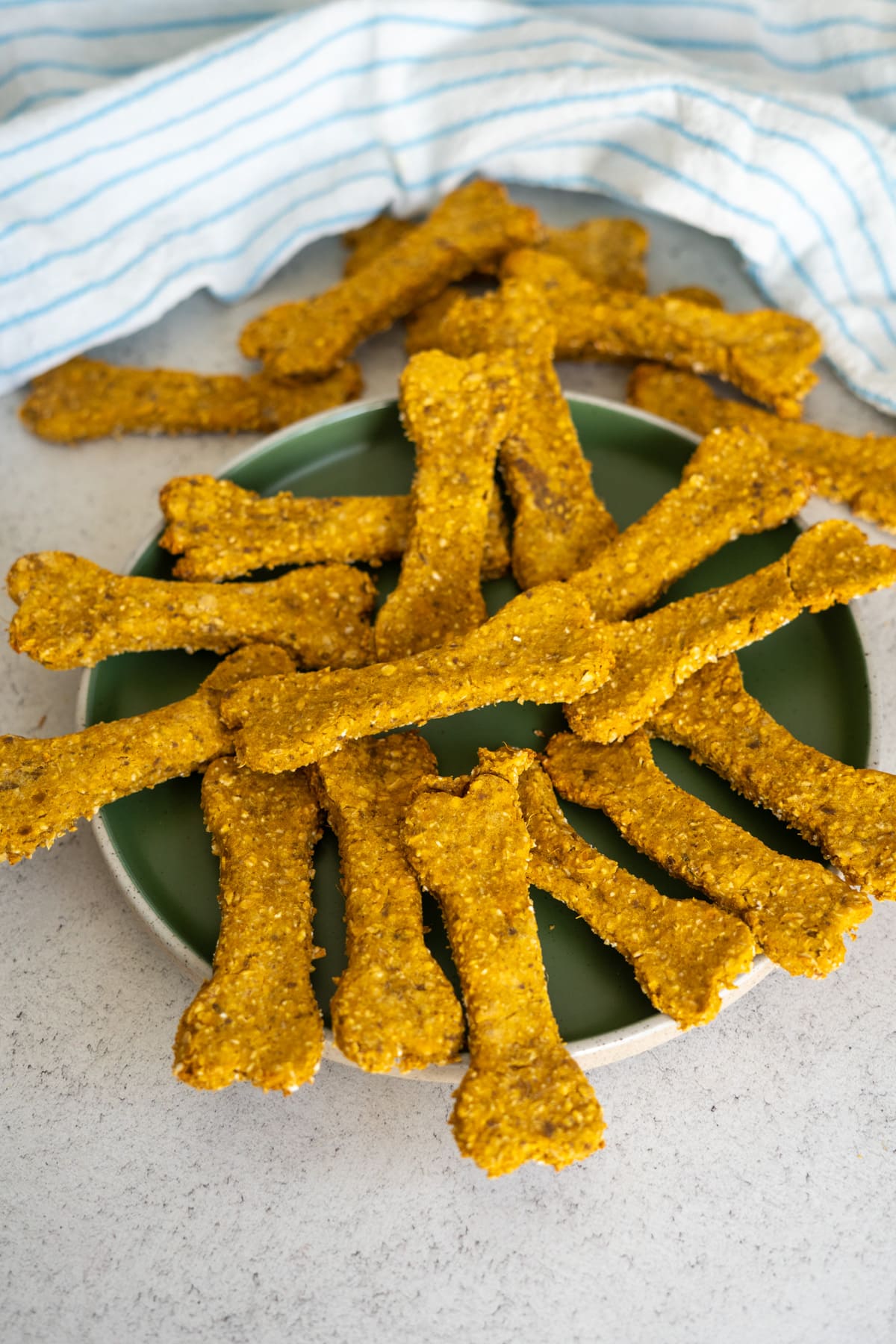 A plate of homemade, bone-shaped duck liver dog treats sits on a countertop with a striped cloth in the background.