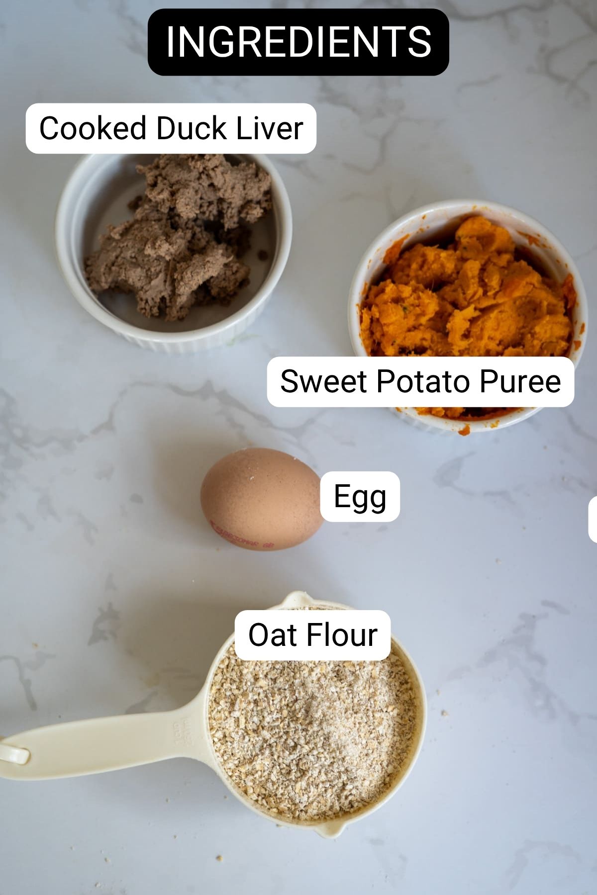 Four labelled ingredients on a white surface: cooked duck liver in a ramekin, sweet potato purée in a bowl, a whole egg, and a measuring jug filled with oat flour.