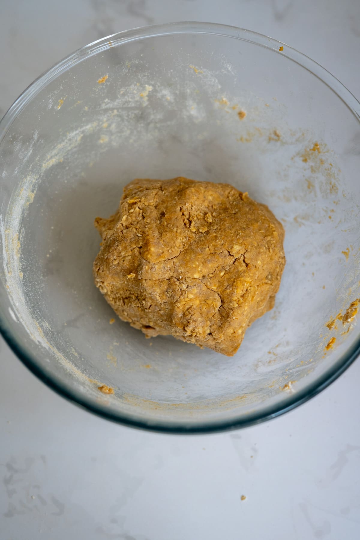 A ball of dough sits in a clear glass mixing basin on a light-coloured surface.