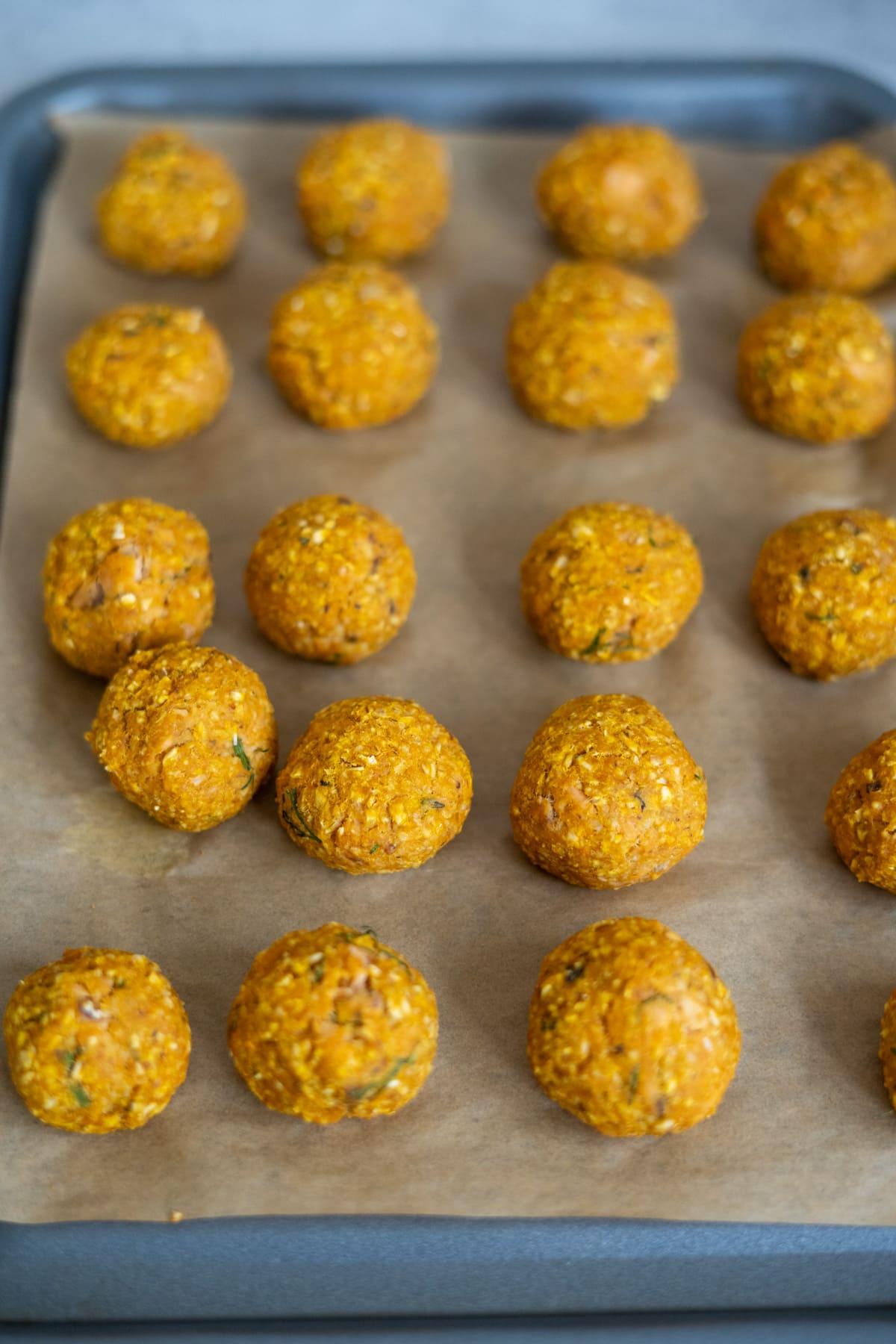 Unbaked falafel balls arranged on a baking tray lined with greaseproof paper, ready to be cooked, much like preparing homemade salmon meatballs for dogs.