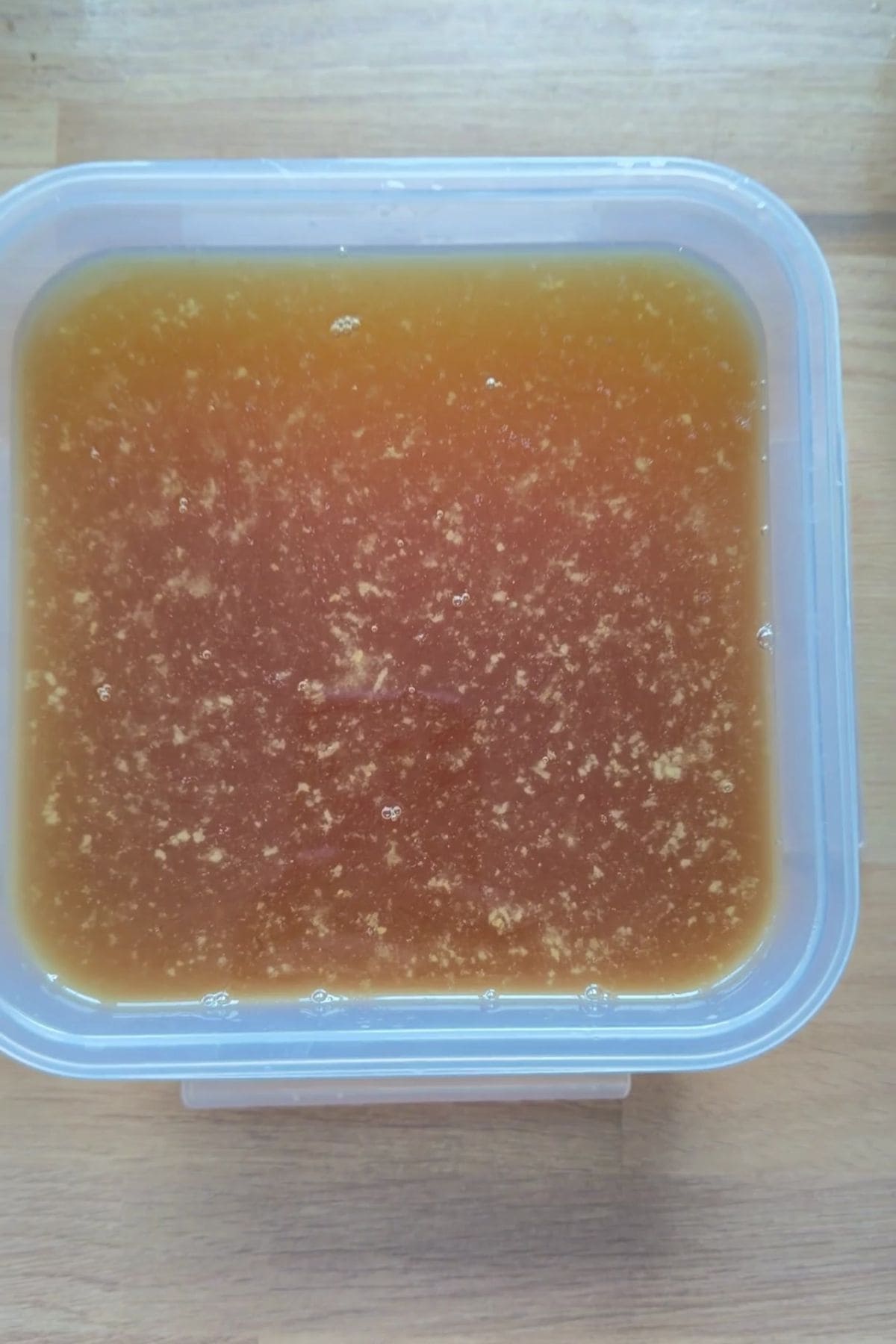 A plastic container filled with beef bone broth for dogs, its brown liquid brimming with visible particles, sits on a wooden surface.